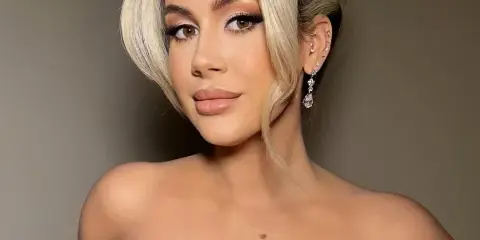 A woman with an elegant updo hairstyle, diamond headpiece, and full bridal makeup wearing a white floral wedding dress.