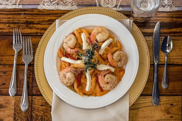 A plated pasta dish with shrimp and cheese served on a formal dining table setting.