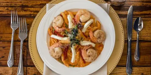 A plated pasta dish with shrimp and cheese served on a formal dining table setting.