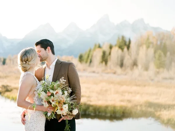 A bride and groom embracing in a field with a mountain range in the background.