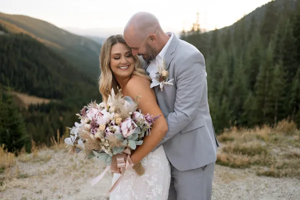A bride and groom embracing outdoors with a mountainous landscape in the background.