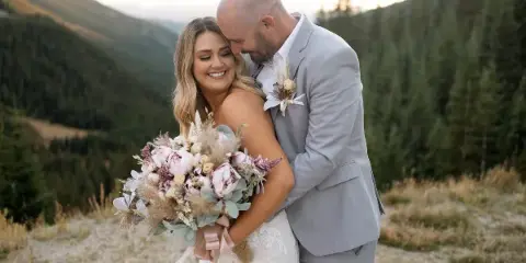 A bride and groom embracing outdoors with a mountainous landscape in the background.