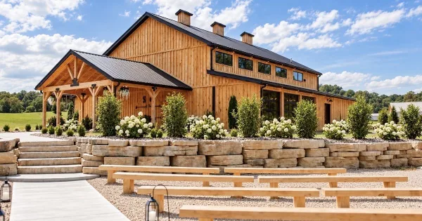 Exterior view of a large wooden wedding venue with a covered porch, stone retaining walls, and outdoor benches.