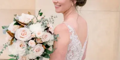 A bride in a white lace dress with an elegant updo hairstyle holding a bouquet of white and blush roses.