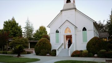Bride and groom standing at the entrance of a white wedding chapel on their wedding day.