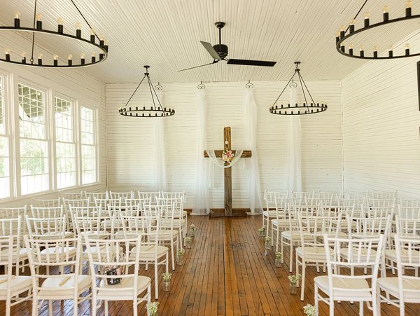 Interior of a white-walled event space with hardwood floors, set up with white chairs for a wedding ceremony.