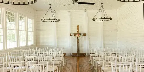 Interior of a white-walled event space with hardwood floors, set up with white chairs for a wedding ceremony.