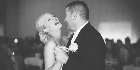A bride and groom laughing and dancing together at a wedding reception.