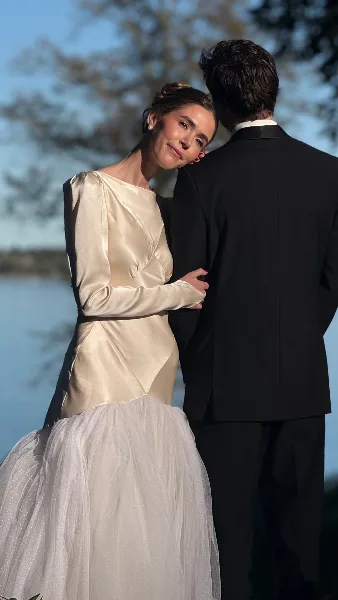 A bride with an elegant updo hairstyle and makeup leaning affectionately against her groom in a suit.