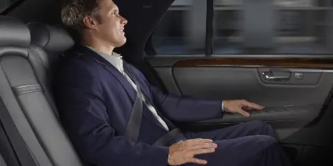 A man in a business suit sitting in the back seat of a luxury car.
