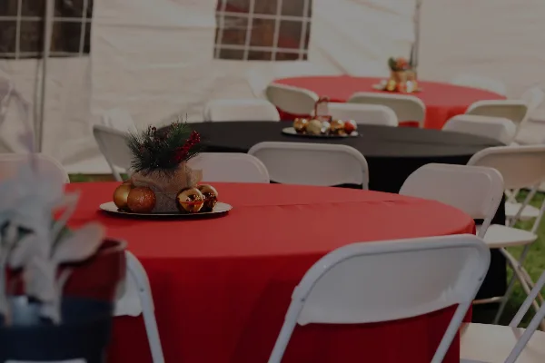 Event setup featuring a white tent, round tables with red and black tablecloths, and white folding chairs.