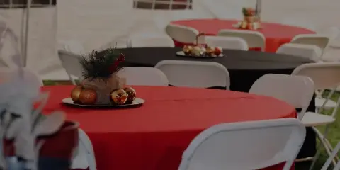 Event setup featuring a white tent, round tables with red and black tablecloths, and white folding chairs.