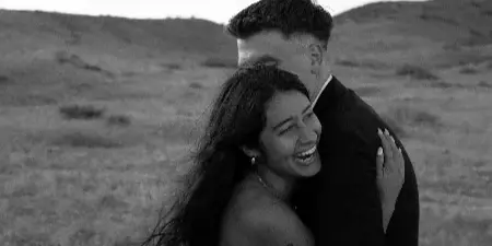 A black and white photograph of a bride and groom embracing in a grassy field.