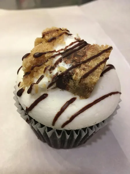 A close-up of a frosted cupcake topped with a piece of baked good and chocolate drizzle.