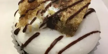 A close-up of a frosted cupcake topped with a piece of baked good and chocolate drizzle.