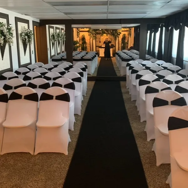 Interior view of a wedding chapel with rows of white chairs, a black aisle runner, and a decorated altar area.
