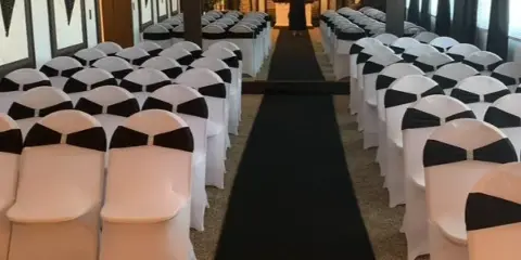 Interior view of a wedding chapel with rows of white chairs, a black aisle runner, and a decorated altar area.