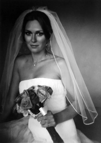 Black and white portrait of a bride in a white dress and veil holding a bouquet of roses.