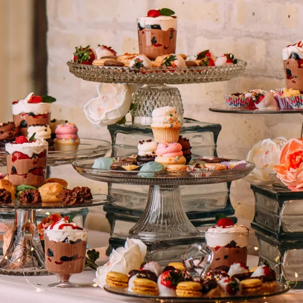 A catering dessert display featuring macarons, cupcakes, and other sweets arranged on glass stands.