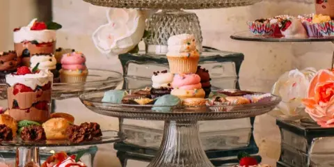 A catering dessert display featuring macarons, cupcakes, and other sweets arranged on glass stands.