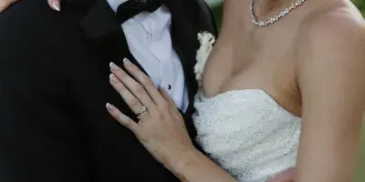 A bride with a styled updo and a groom in a tuxedo embracing outdoors.
