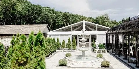 Outdoor wedding venue courtyard featuring a white tent, stone building, fountain, and manicured gardens.