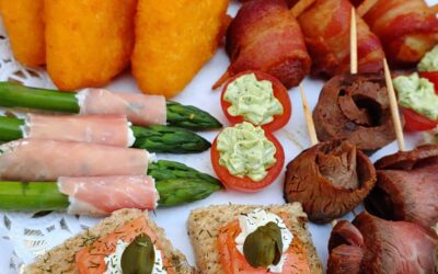 A close-up view of a catering buffet table featuring asparagus wrapped in prosciutto, stuffed mushrooms, and salmon crostini.
