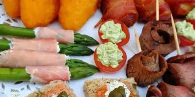 A close-up view of a catering buffet table featuring asparagus wrapped in prosciutto, stuffed mushrooms, and salmon crostini.
