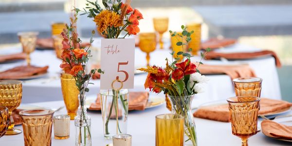 A wedding table setting featuring white linens, amber glassware, and orange floral centerpieces.