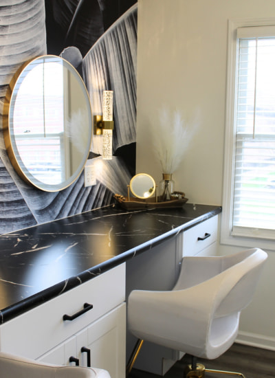 Interior view of a salon styling station featuring a black marble counter, a round gold-framed mirror, and a white chair.