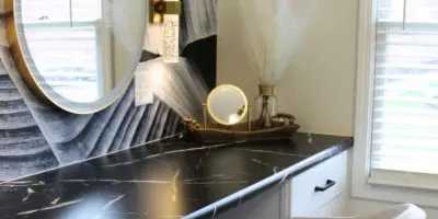 Interior view of a salon styling station featuring a black marble counter, a round gold-framed mirror, and a white chair.