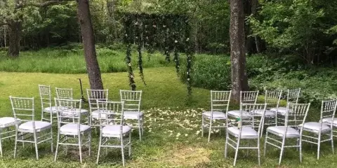 An outdoor wedding ceremony setup with white Chiavari chairs arranged on a lawn facing a floral arch.