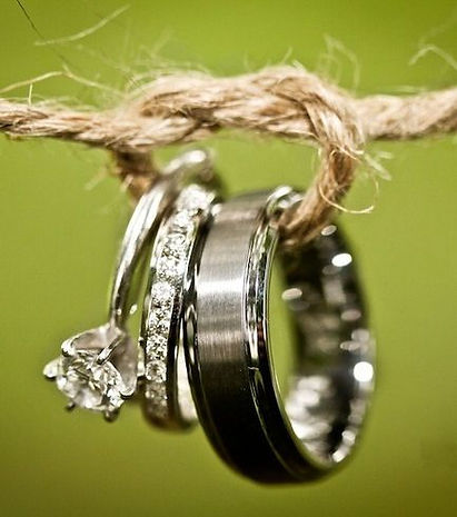 Wedding rings, including an engagement ring and bands, hanging from a piece of twine against a green background.