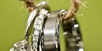 Wedding rings, including an engagement ring and bands, hanging from a piece of twine against a green background.