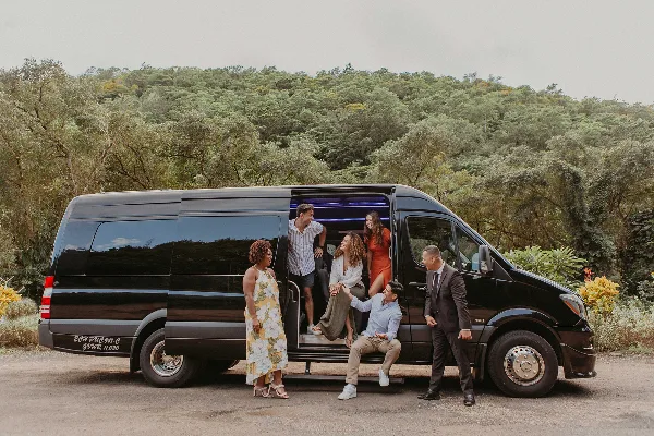 A group of people boarding a black passenger van with 'EC HAWAII' branding on the side, parked in a scenic outdoor location.