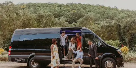A group of people boarding a black passenger van with 'EC HAWAII' branding on the side, parked in a scenic outdoor location.