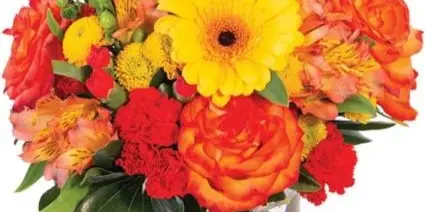 A vibrant floral arrangement in a clear glass vase featuring yellow gerbera daisies, orange roses, and red carnations.