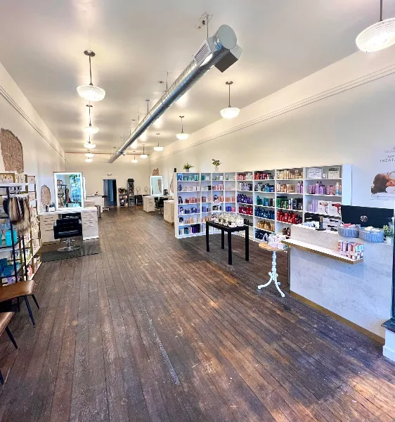 Interior view of a hair salon with wooden floors, styling stations, and shelves stocked with hair products.