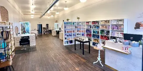 Interior view of a hair salon with wooden floors, styling stations, and shelves stocked with hair products.