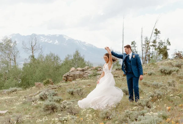 A bride and groom dancing in a mountainous field with snow-capped peaks in the background.