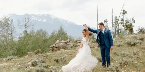 A bride and groom dancing in a mountainous field with snow-capped peaks in the background.