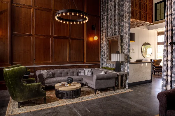 Interior view of The Louis Hotel lobby featuring a grey sectional sofa, green armchair, wood paneling, and a chandelier.