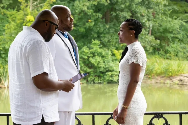 A bride and groom standing outdoors near a body of water, with the groom holding a tablet.
