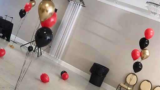A balloon arrangement featuring red, black, and gold balloons set up in an event venue.
