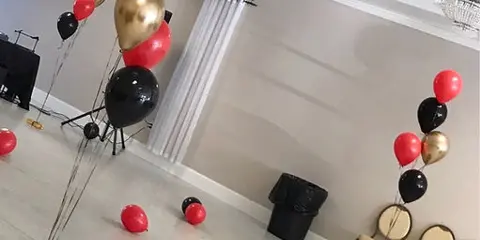 A balloon arrangement featuring red, black, and gold balloons set up in an event venue.