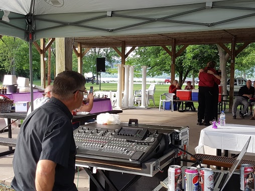 A sound engineer operating a mixing console at an outdoor event under a canopy.