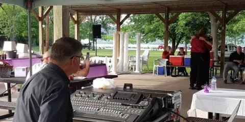 A sound engineer operating a mixing console at an outdoor event under a canopy.