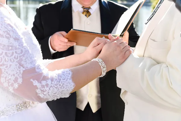 A wedding officiant holds a book while a bride and groom exchange rings during a ceremony.