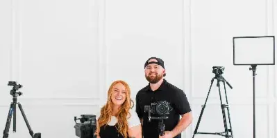 A man and a woman holding professional cameras and lenses in a studio with photography equipment.