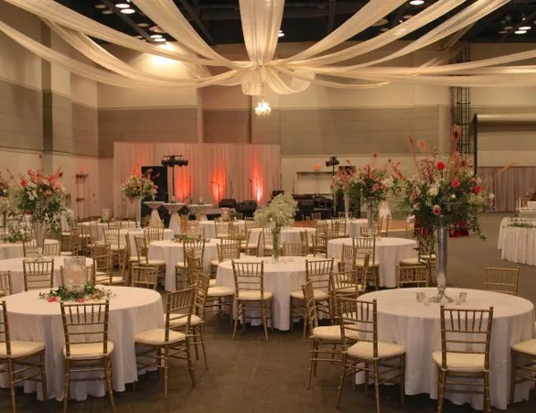 A spacious event hall set up for a wedding reception with round tables, white linens, and floral arrangements.